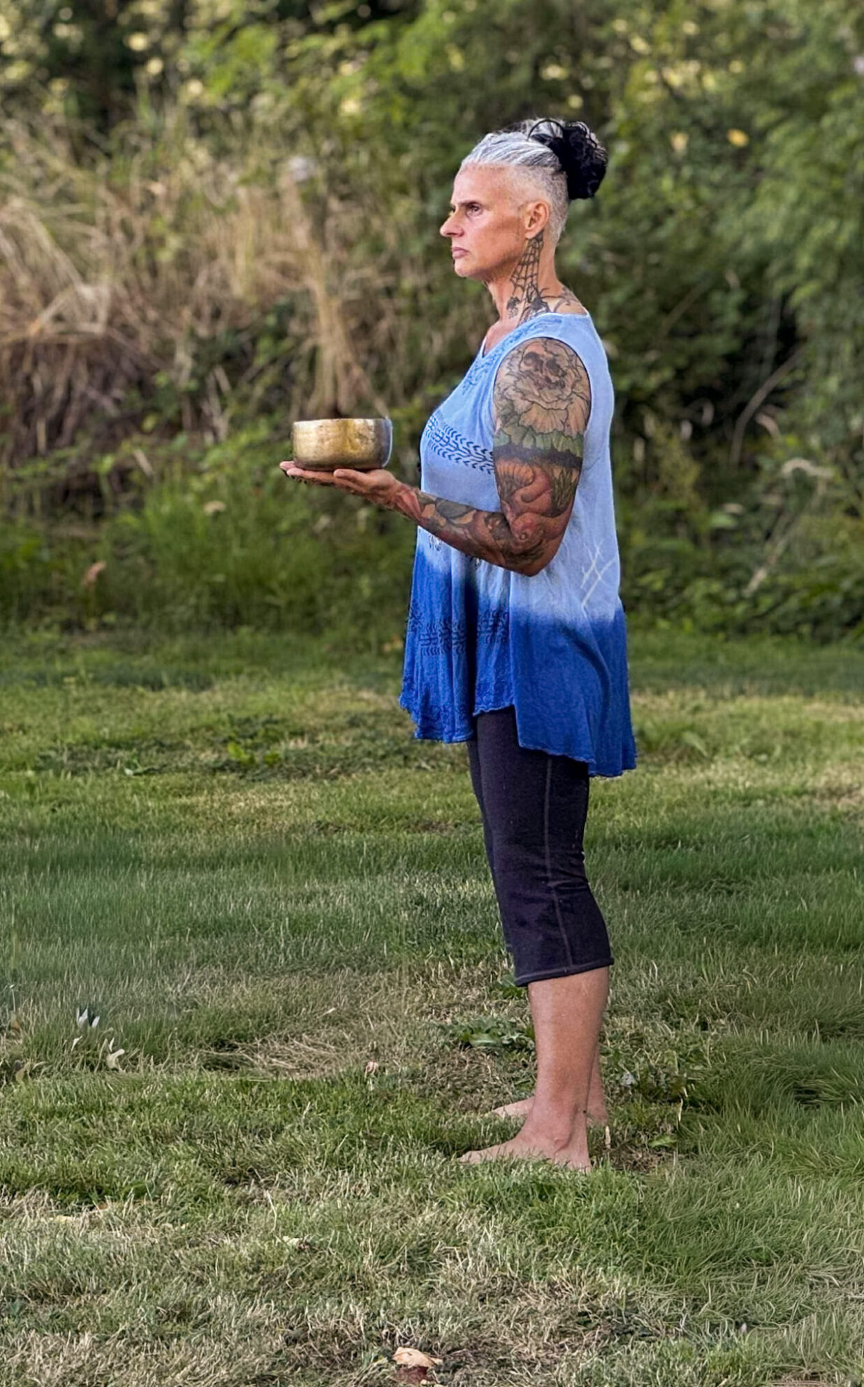 Athena stands on the grass with a tibetan bowl in her left hand. she stares off into the distance